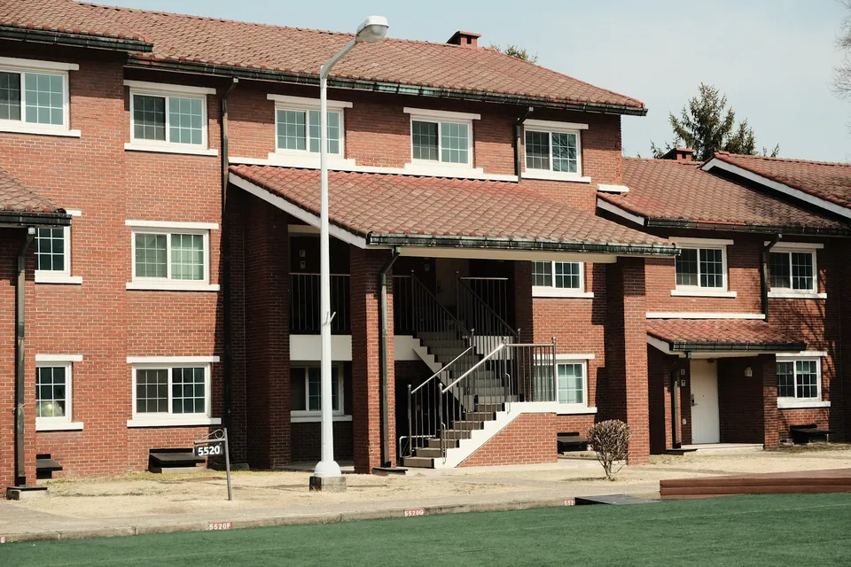 Illustrative photograph: Red brick residential building with an exterior staircase, white-framed windows and lawn